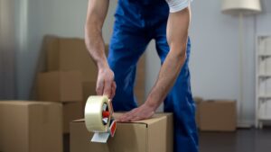 A person applying packing tape to a cardboard box while preparing for a move.