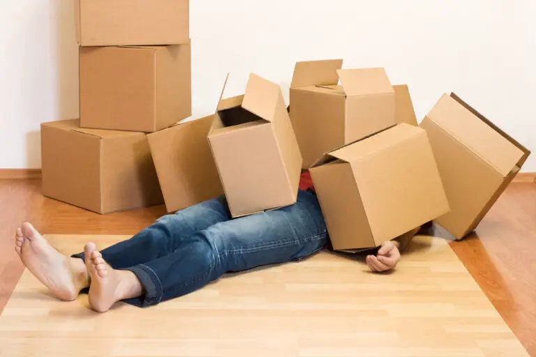 Individual lying on the floor with cardboard boxes stacked around them in a room.